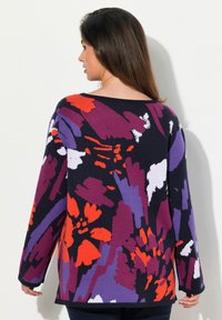 Stickad tröja med ett färgglatt blommönster i röd, lila, vit och svart. Den har en vid halsringning och långa ärmar.