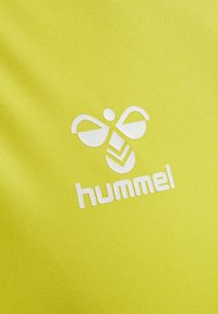 Weißes stilisiertes Bienenlogo mit dem Schriftzug „hummel“ auf hellgelbem, texturiertem Stoffhintergrund.