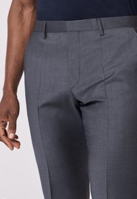 Graue maßgeschneiderte Hose aus glattem Stoff, mit flachem Bund, seitlichen Taschen und schlanker Passform. Mit Gürtelschlaufen akzentuiert.
