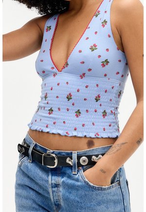 Lyseblå, cropped tanktop med rød jordbærprint, V-hals design, tekstureret stof og flæser nederst. Båret med høj talje denim jeans.