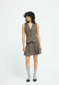 Braun gestreiftes Weste-Kleid mit tailliertem Oberteil, Peplum-Taille und gürtelt Detail. Kombiniert mit grauen gerippten Socken und schwarzen spitzen Pumps.