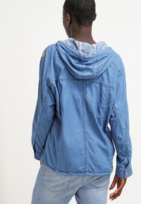 Jeansjacka i ljusblått, med huva och subtil sömnad. Inkluderar en tanfärgad läderpatch och avslappnad passform, med knappade manchetter.