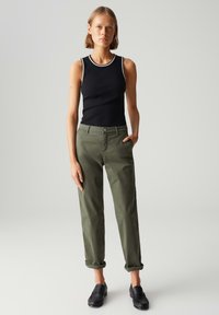 Canottiera nera con bordi bianchi, pantaloni verde oliva arrotolati e scarpe nere slip-on. Design semplice, texture liscia e colori neutri.