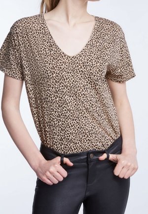T-shirt à imprimé léopard avec un col en V, manches courtes, dans des couleurs beige et marron, associé à un jean noir ajusté, texture de tissu lisse.