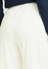 Pantalon de jogging blanc avec une coupe décontractée et une taille élastique, présentant une texture lisse et un design épuré, associé à un haut bleu marine.