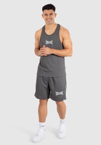 Camiseta sin mangas gris y pantalones cortos a juego con el logo "SMILODOX" en blanco. La tela tiene una textura acanalada. Se lleva con zapatillas blancas.