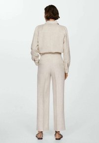 Chemise en lin beige et pantalon large avec un détail de poche arrière. Texture lisse avec une coupe décontractée. Sandales à fines lanières.