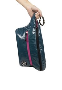 Bolso de tela brillante color verde azulado con un zipper negro y un zipper de acento rosa. Incluye una cadena como asa y un parche redondo con el logo en la parte frontal.