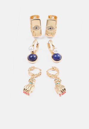 Trois paires de boucles d'oreilles dorées : l'une avec un design géométrique et des accents transparents, l'autre avec une pierre bleue et une perle, et la dernière avec un motif de main.