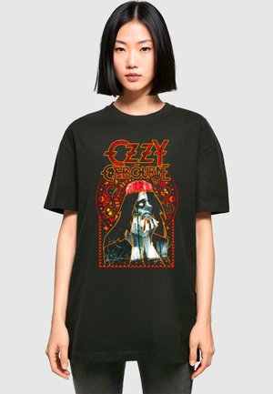 Schwarzes, oversized T-Shirt mit leuchtendem Grafikdruck einer Figur mit einem roten Stirnband, umgeben von dekorativen Elementen in Orange und Weiß.