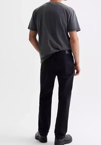 T-shirt di cotone grigio con maniche corte, abbinato a jeans di denim neri. L'outfit presenta una vestibilità comoda e dettagli minimi. Calzature nere.