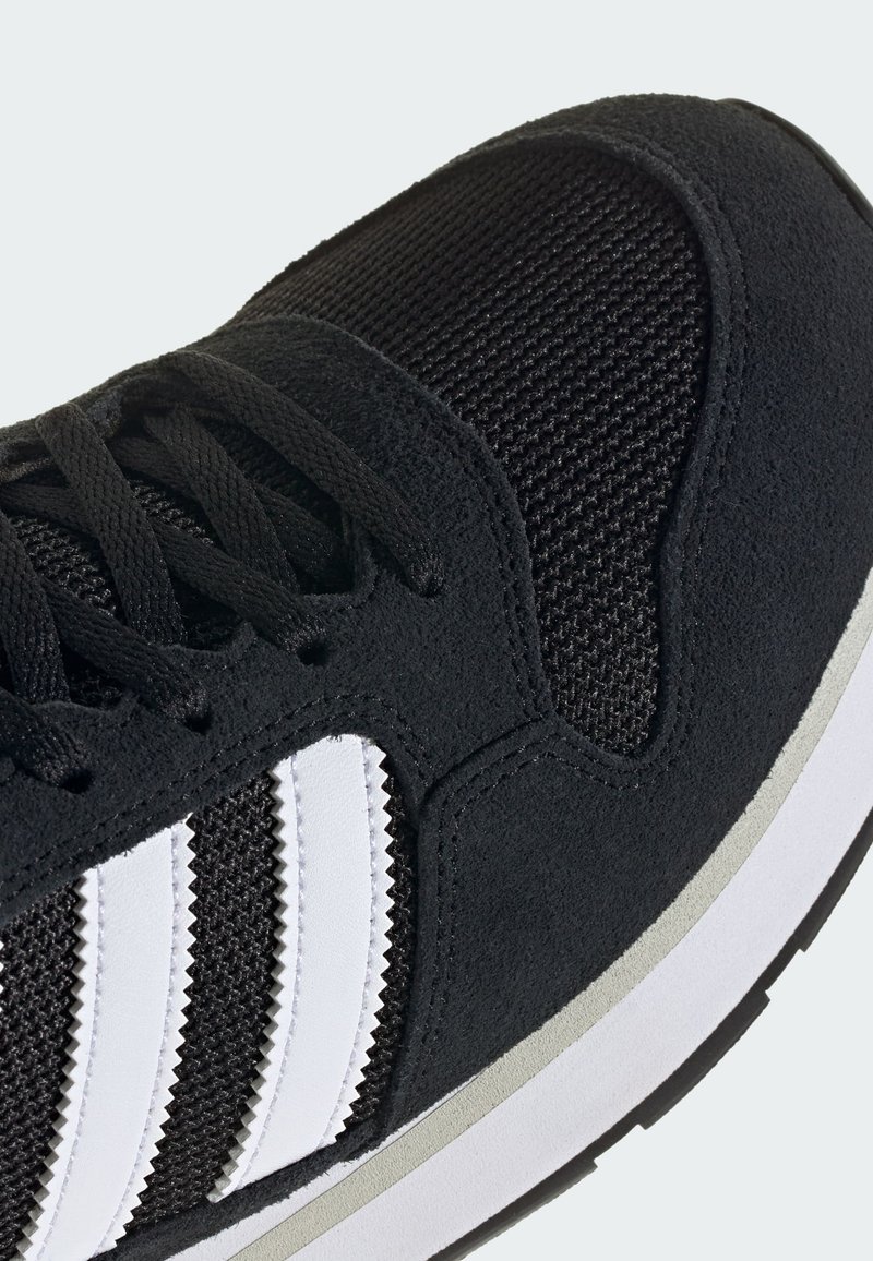 Black athletic shoe with white three stripes on the side, black laces, mesh upper, and white and gray sole detail.