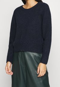 Granatowy sweter z okrągłym dekoltem i długimi rękawami. Wykonany z miękkiej, teksturowanej tkaniny, o luźnym i krótki kroju.