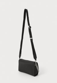 Black rectangular bag made of soft material, featuring a detachable strap and silver chain accent. Smooth texture with minimal detailing.
