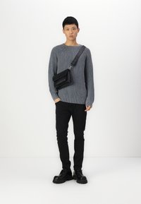 Grå ruggad tröja med rund halsringning, svart axelremsväska, svarta slim-fit byxor och svarta skor med tjock sula. Enkelt, minimalistisk design.
