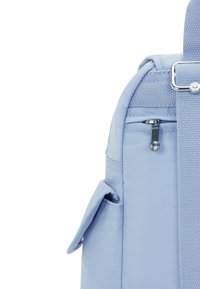 Mochila de tela azul claro con un bolsillo con cremallera, un bolsillo lateral y una correa texturizada. Textura suave con costuras limpias y hardware minimalista.