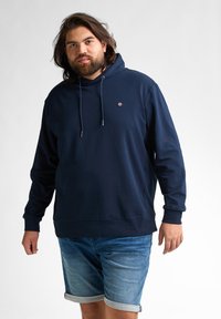 Hanorac din bumbac de culoare albastru marin, cu buzunar frontal, glugă ajustabilă cu șnur și un mic logo pe piept. Purtați-l cu pantaloni scurți din blugi.