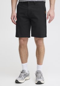Sorte bomulds shorts med lige ben, forlommer og et brunt lædermærke på højre side. Stylret med grå træningssko og hvide sokker.