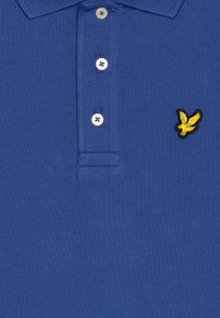 Mėlynas polo marškinėlis, pagamintas iš tekstūrinės medžiagos, su trimis mygtukais ir geltonu siuvinėtų paukščio logotipu kairėje krūtinės pusėje.