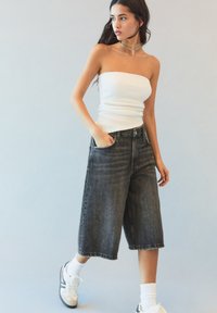Culottes en denim noir avec une coupe décontractée, taille haute, et poches avant, associés à un top sans manches à rayures blanches et des baskets blanches.