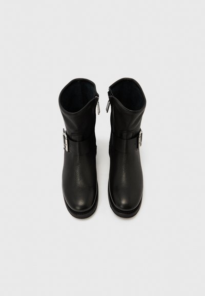 Fekete bőr bokacsizma texturált felülettel, oldalsó cipzárral és egy ezüst csatos pánttal a felső részen.