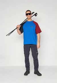 Dual-colored short-sleeve t-shirt (blue and burgundy) featuring a logo, paired with dark cargo pants and sturdy black hiking boots.