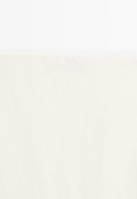 Ciotola di ceramica bianca riempita di mirtilli freschi su una superficie bianca e strutturata con un panno bianco accanto.