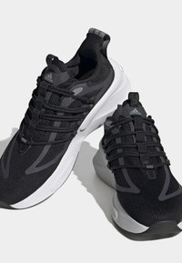 Baskets de sport noires avec une tige en maille respirante, présentant des accents réfléchissants et des lacets élastiques. Semelle intermédiaire blanche épaisse pour l'amorti.
