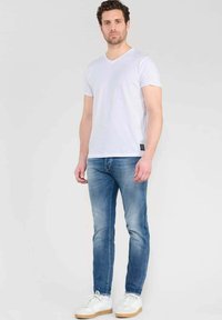 T-shirt bianca a maniche corte con scollo a V, abbinata a jeans blu slim-fit. Calzature: sneakers bianche con suola beige. Look semplice e casual.