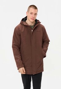 Veste imperméable marron avec capuche, fermeture éclair à l'avant et deux poches latérales. Présente une texture lisse et des poignets élastiques. Doublure noire visible.