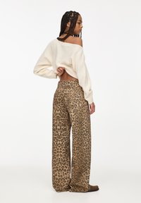 Kremast pulover s širokimi rokavi in off-shoulder obliko; v kombinaciji z leopardjim potiskom, hlačami širokega kroja z visokim pasom.