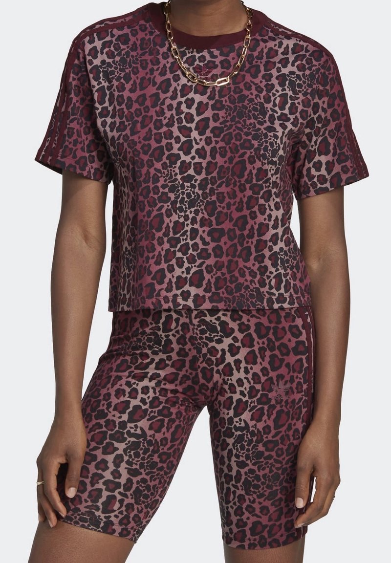Persona con camiseta y pantalones cortos de motorista a juego en estampado de leopardo en granate y negro, complementados con un grueso collar de cadena dorada.