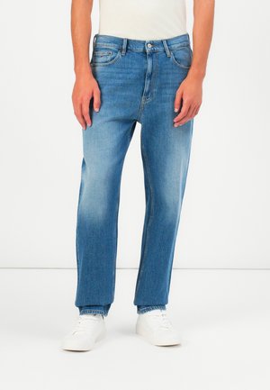 Blue denim jeans featuring a straight cut, lighter wash with fading, five-pocket design, and a button-fly closure. Paired with white sneakers.