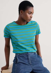 Camiseta a rayas en algodón de color verde claro y azul, de mangas cortas y escote redondo, combinada con pantalones cortos de denim. Textura suave y ajuste casual.