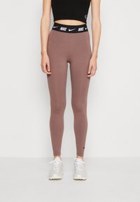 Nike tajice u mauve boji s crnim elastičnim pojasom koji sadrži bijeli logotip. Glatka tekstura, kroj koji se prilagođava tijelu, potpuno dužina.