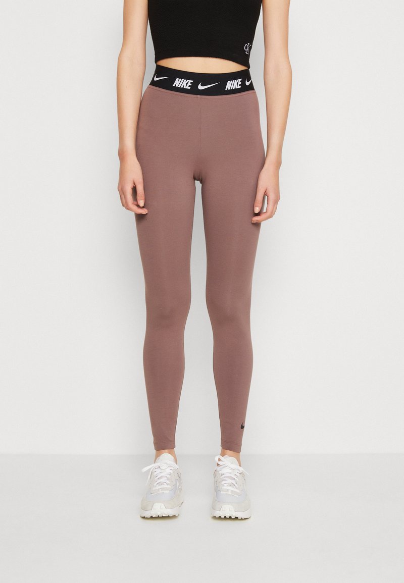 Nike tajice u mauve boji s crnim elastičnim pojasom koji sadrži bijeli logotip. Glatka tekstura, kroj koji se prilagođava tijelu, potpuno dužina.