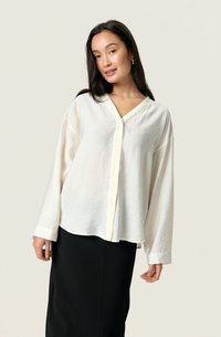 White long-sleeve button-up shirt with a V-neck, soft textured fabric, and a relaxed fit, paired with a black pencil skirt.