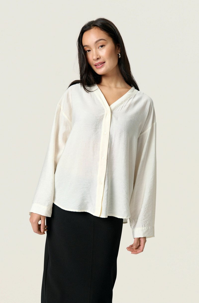 White long-sleeve button-up shirt with a V-neck, soft textured fabric, and a relaxed fit, paired with a black pencil skirt.
