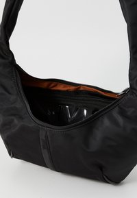 Borsa a spalla nera in nylon con una texture morbida, chiusura con zip e un interno marrone a contrasto. Contiene un piccolo scomparto con zip all'interno.