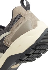 Der Sneaker verfügt über ein Obermaterial aus braunem Wildleder und grauem Mesh, eine Gummisohle und eine strukturierte schwarze Außensohle mit ausgeprägten Stollen für Traktion.