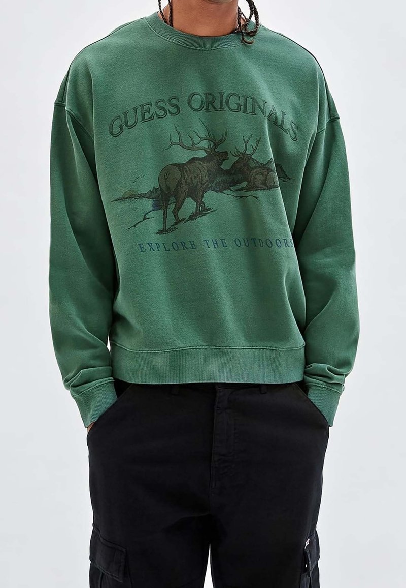 Groene sweatshirt met ronde hals, voorzien van een bedrukt ontwerp van een eland en tekst. Geribbelde boorden en zoom, gemaakt van zacht materiaal.