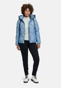 Jasnoniebieska, pikowana kurtka puchowa z kapturem, szary sweter, czarne spodnie i białe sznurowane buty. Posiada kontrastujące sznurki i przeszycia.