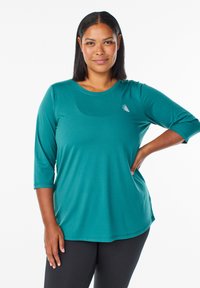 Tyrkysový top s dlhým rukávom, okrúhlym výstrihom a rukávmi po trištvrte. Vyrobený z hladkej, elastickej látky. Obsahuje malé, nenápadné logo na hrudi.