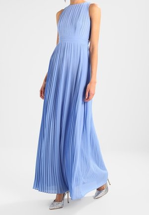 Robe plissée bleu clair sans manches, longueur au sol, portée avec des escarpins à paillettes argentées sur une personne debout.