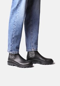 Bottes Chelsea en caoutchouc noir avec un panneau latéral en élastique texturé noir et blanc, dotées d'une semelle épaisse noire et d'une hauteur au niveau de la cheville.