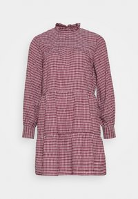 Robe à carreaux rouges et blancs avec un col haut à volants, des manches longues et un ourlet en couches. Fabriquée dans un tissu léger.
