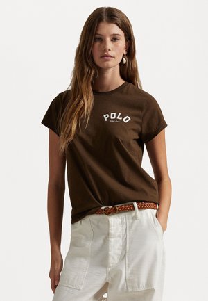 Καφέ βαμβακερό t-shirt με κοντά μανίκια, που διαθέτει λευκό λογότυπο "POLO". Συνδυασμένο με λευκά παντελόνια και πλεκτή καφέ ζώνη.