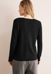 Maglietta nera a maniche lunghe con scollatura a barca, realizzata in un morbido tessuto testurizzato. Il retro presenta un design semplice senza decorazioni.