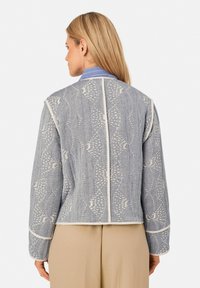 Blauer gemusterter Blazer mit weißen Nähten, im cropped Design, mit kontrastierendem Kragen und cremefarbigen Paspeln entlang der Kanten und Ärmel.