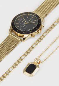 Montre en maille dorée avec cadran noir, accents dorés et fonctionnalités chronographe. Comprend un bracelet en chaîne dorée et un collier en pendentif avec une pierre noire.